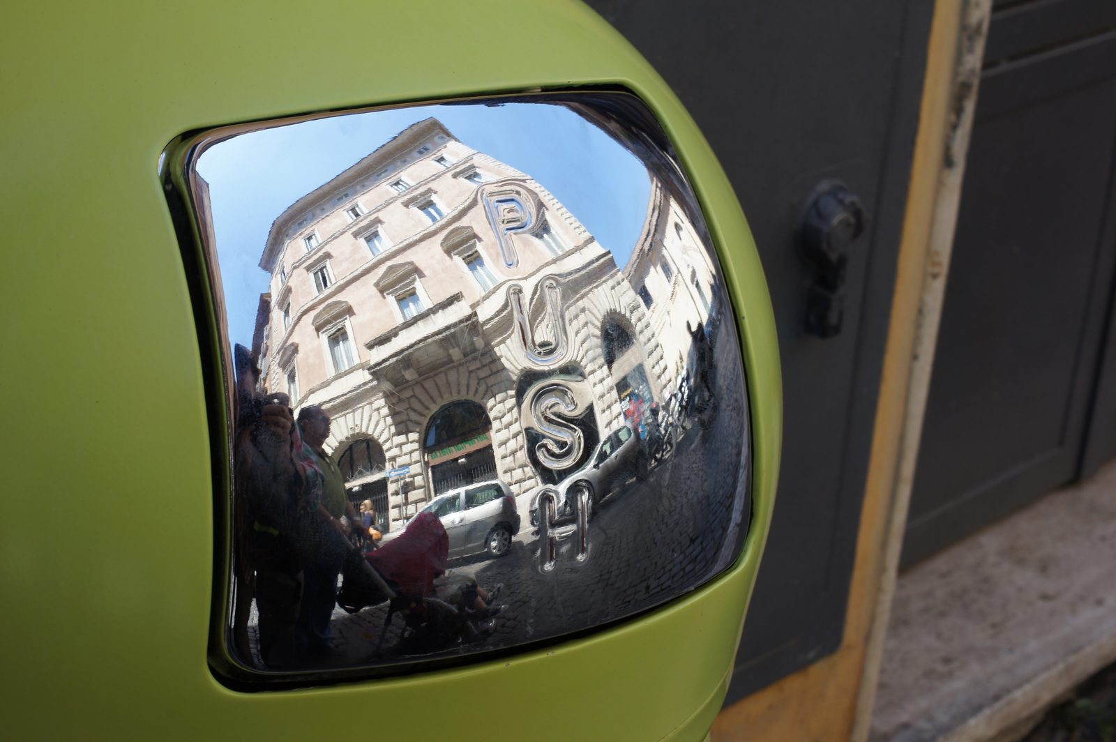 Reflection of a building in a green scooter mirror reading PUSH