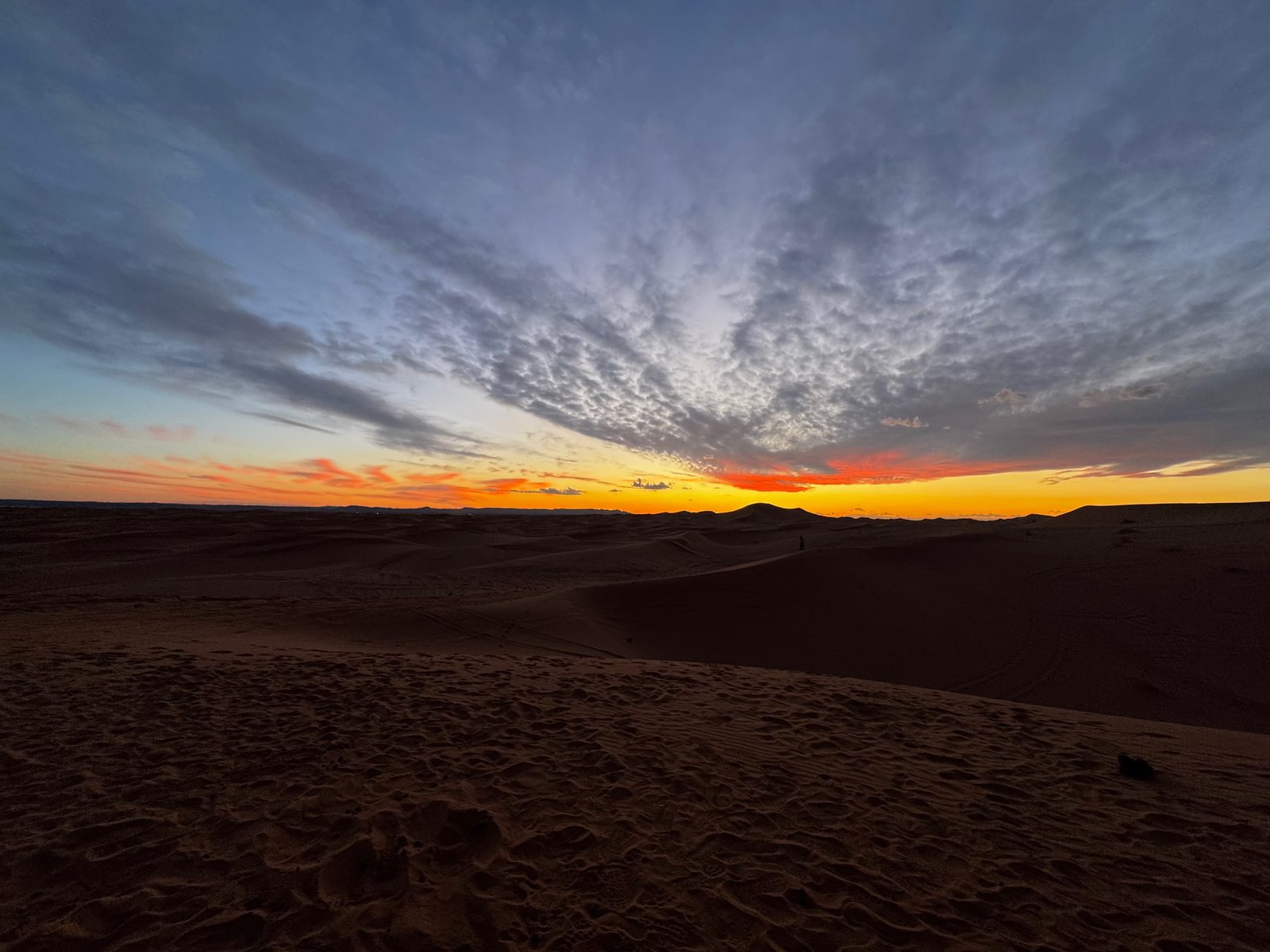 Silhouetted sand dunes under a dramatic sunset sky